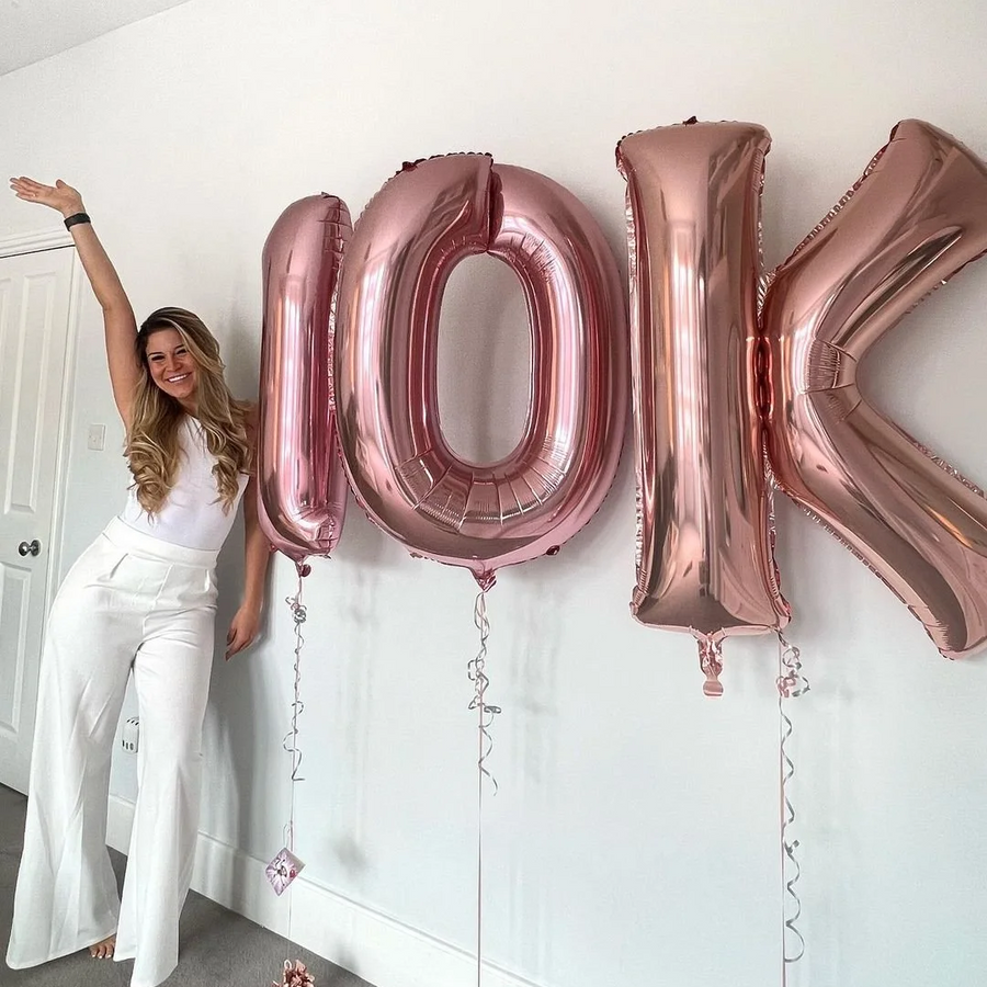 Person with rose gold '10K' balloons against a white wall